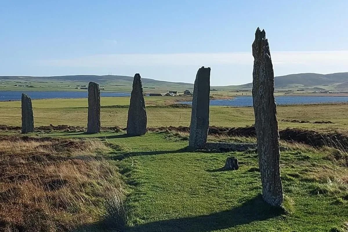 a group of stone pillars in a field with a body of water